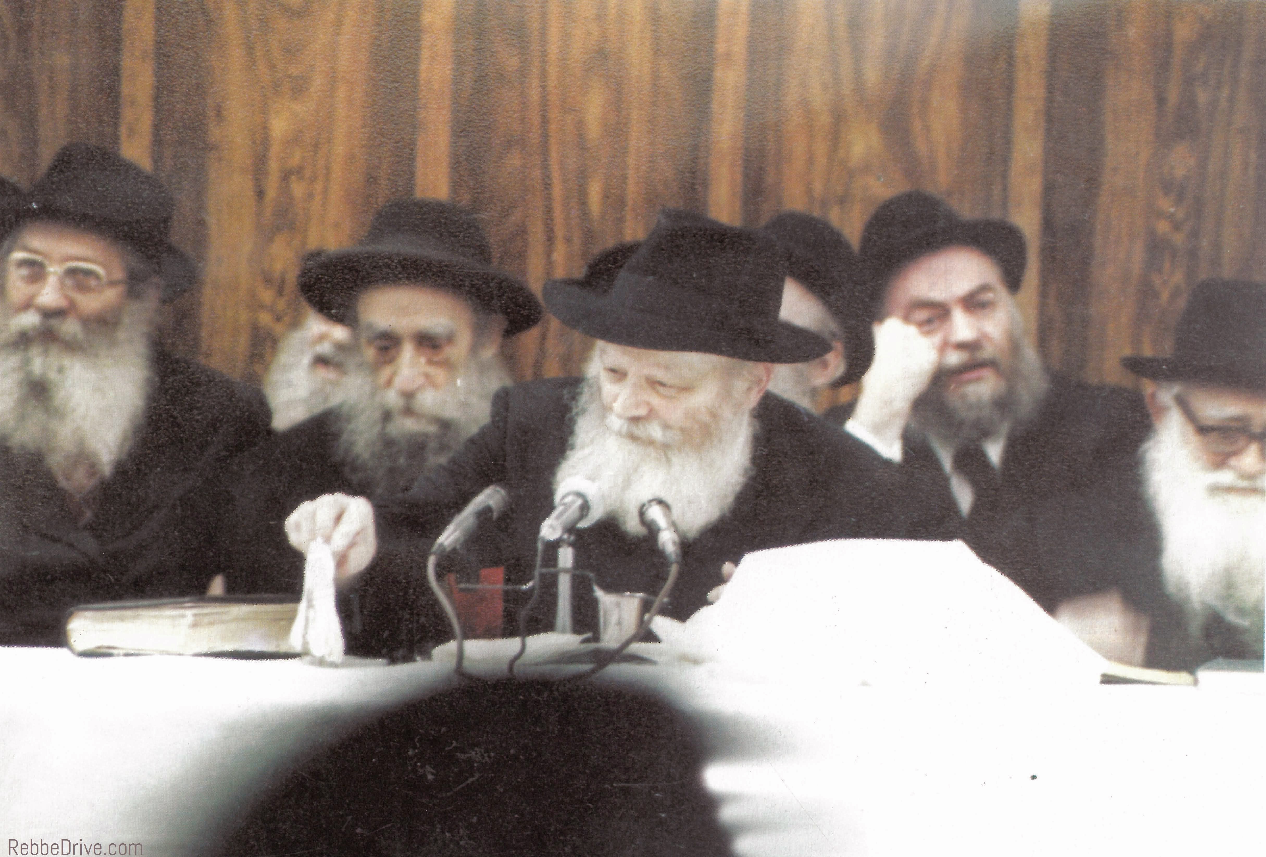 The Lubavitcher Rebbe teaching at a gathering, with open Torah books and microphones before him.